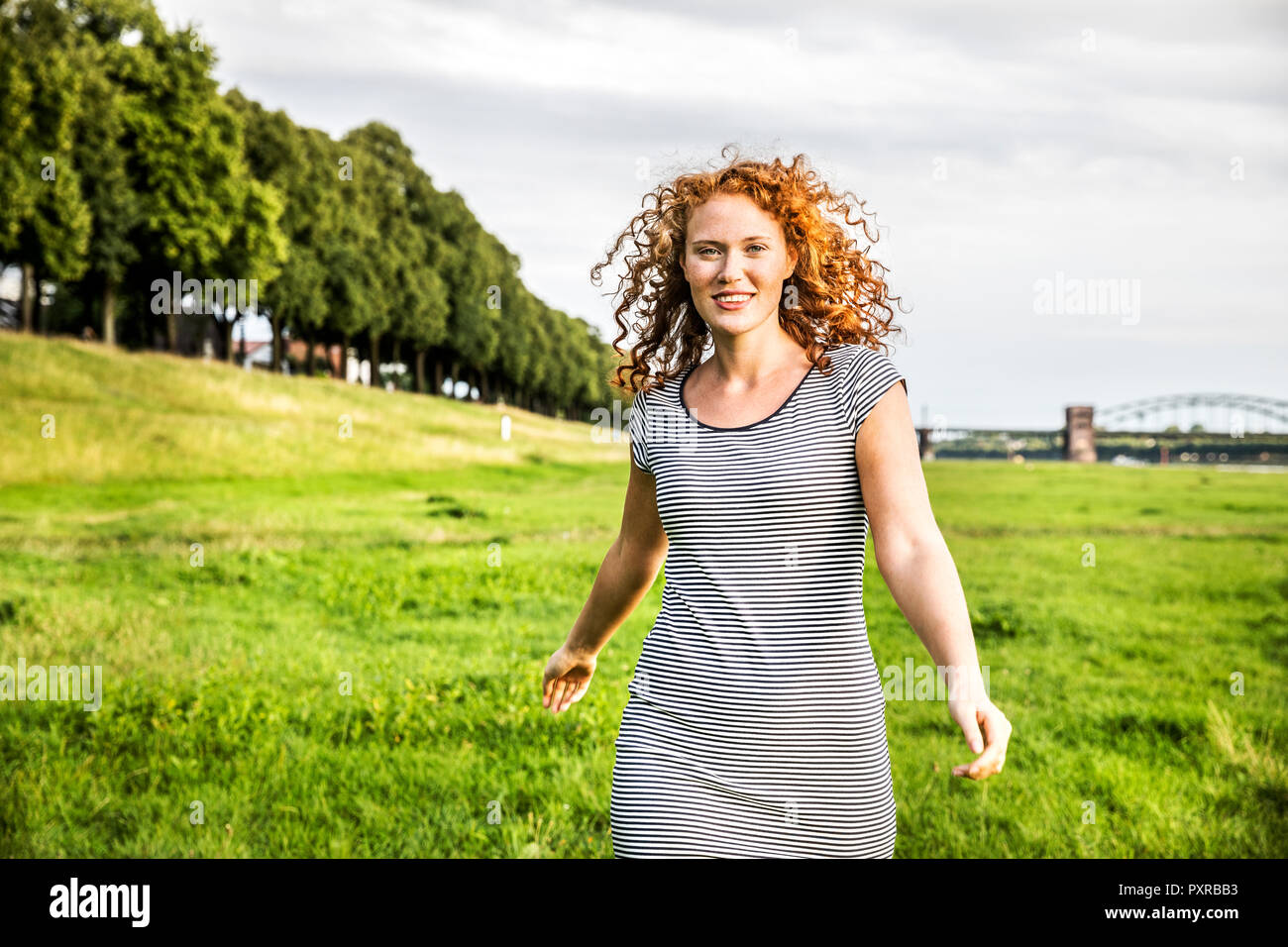 Germany, Cologne, portrait of smiling young woman on meadow Stock Photo