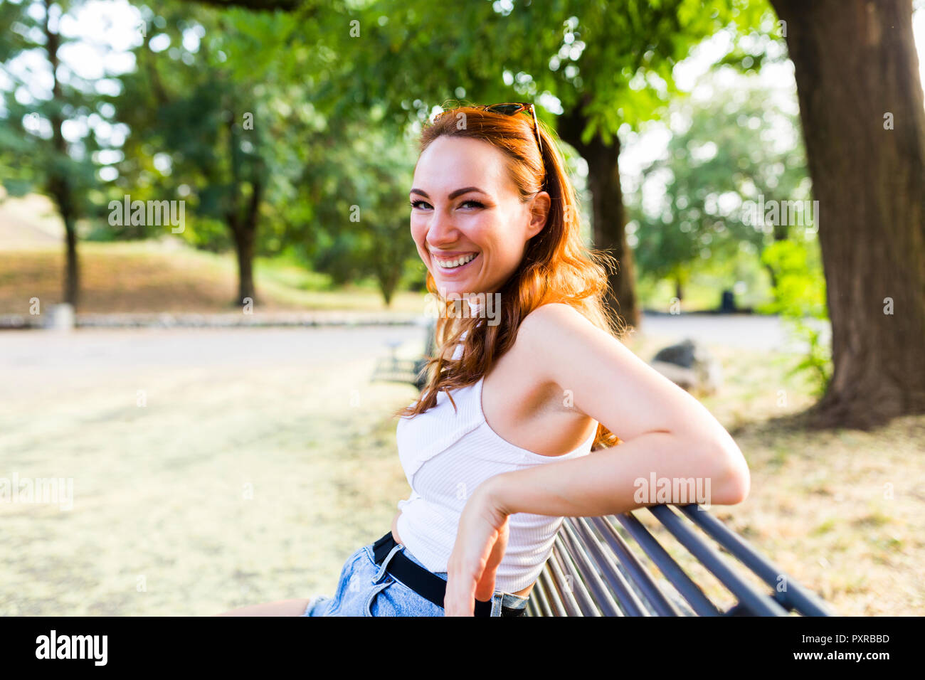 Portrait of laughing redheaded woman sitting on bench in a park Stock ...