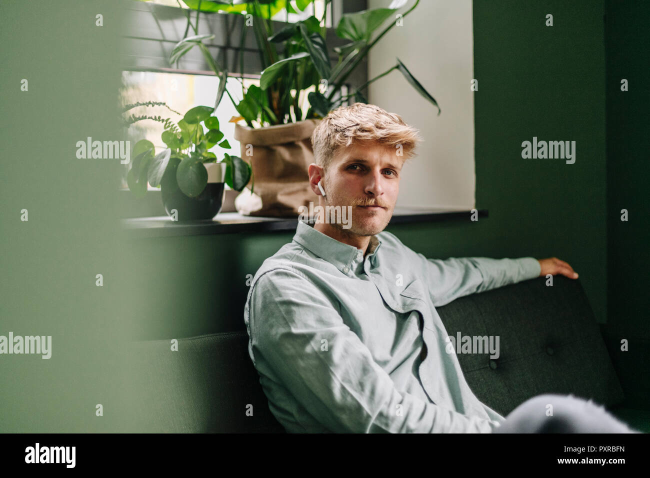 Young man sitting on green couch, using ear buds Stock Photo