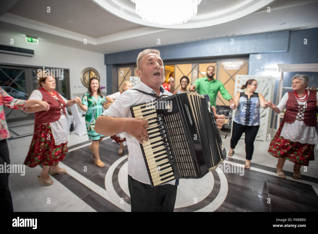 Adult male senior sings and plays the accordion as group of people dance in circle around him,  Zwoleń, Masovian Voivodeship, Poland Stock Photo