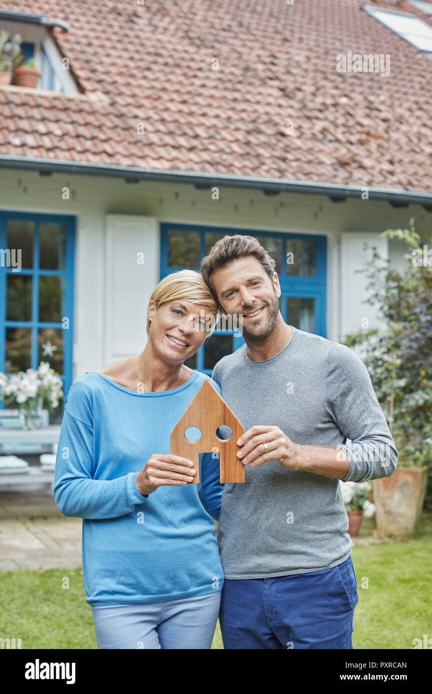 Portrait of smiling couple standing in front of their home holding house model Stock Photo