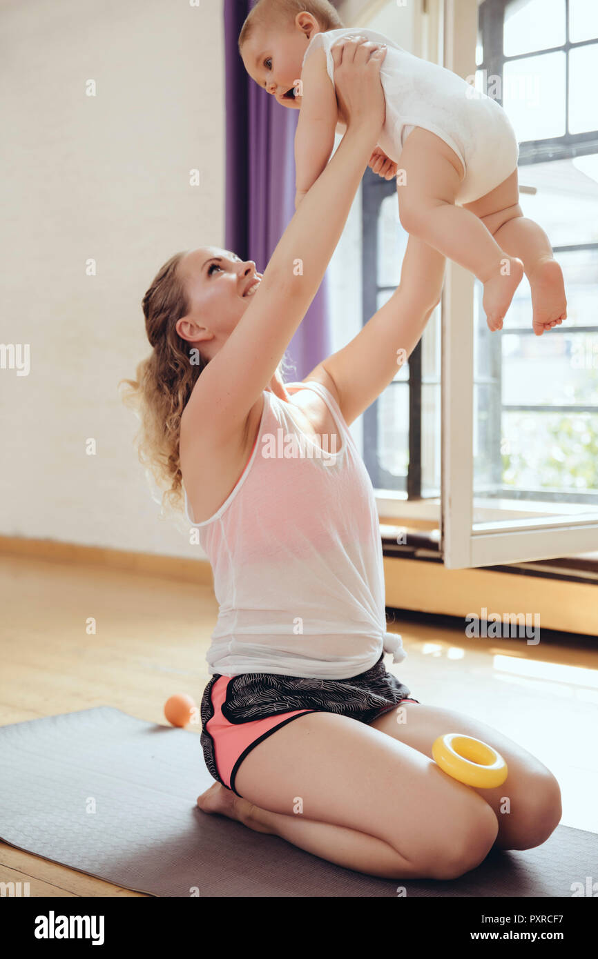 Mother holding up her baby while working out on a yoga mat Stock Photo