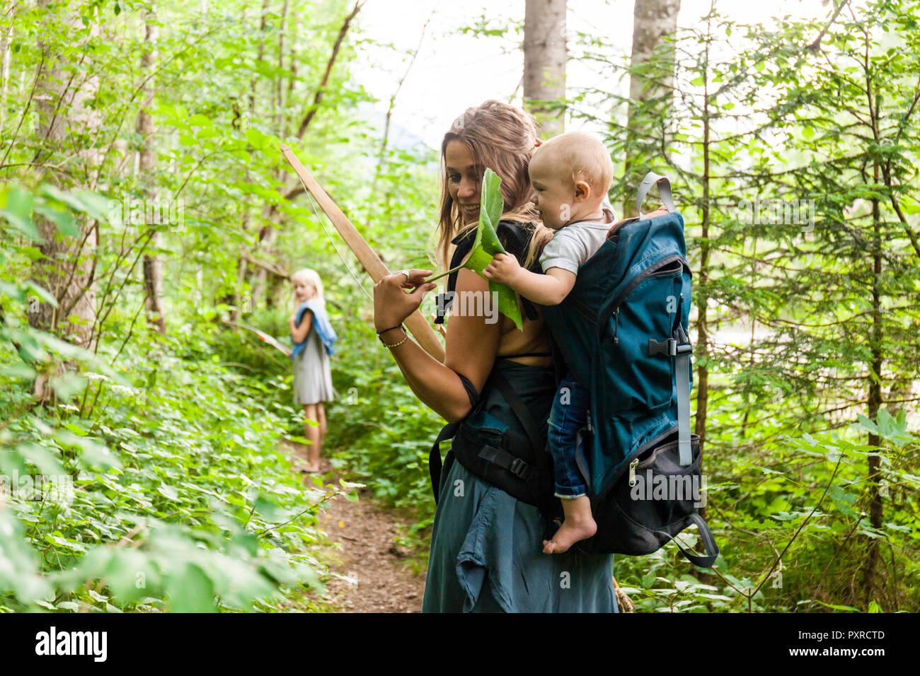 Woman hiking in the woods showing large leaf to baby boy in backpack Stock Photo