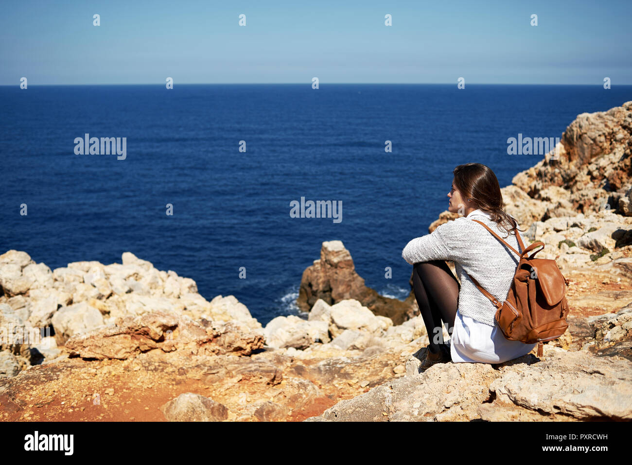 Young brunette woman sitting on coast, looking at view Stock Photo