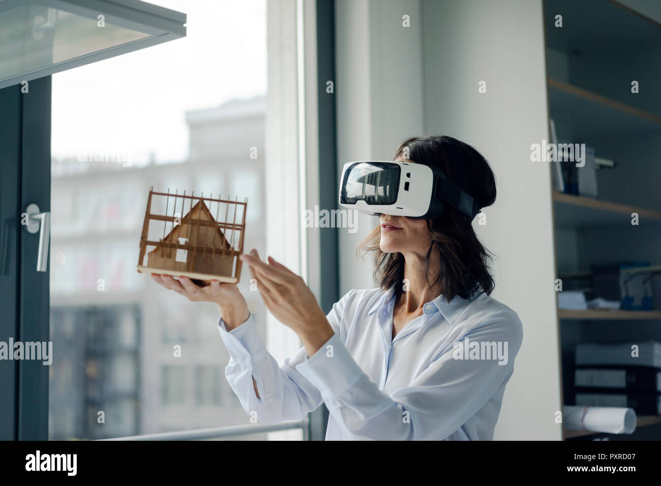 Woman holding architectural model of house, using VR glasses Stock Photo
