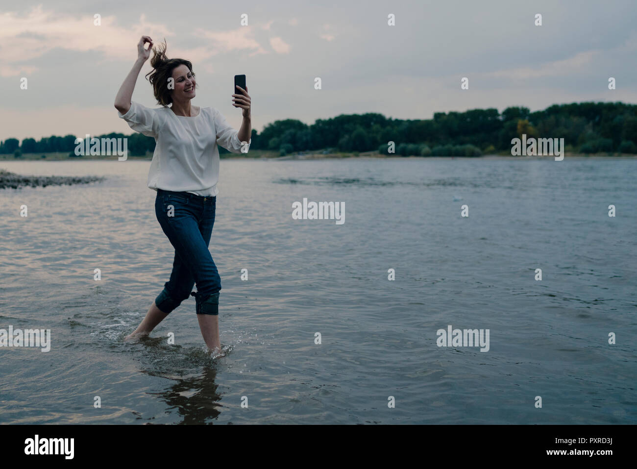 Laughing woman running at the riverside, using smartphone Stock Photo