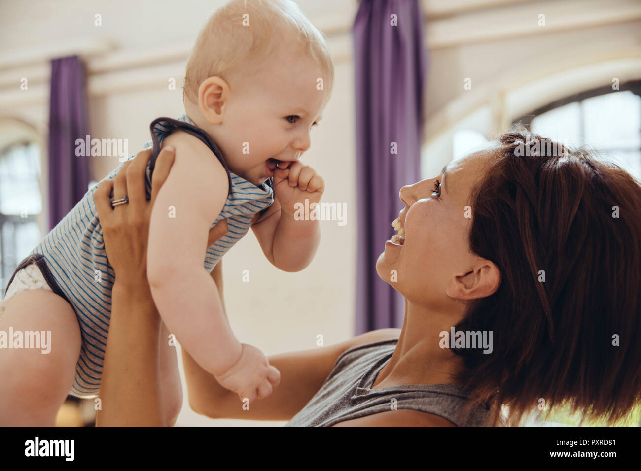 Sporty woman lifting up happy baby in training room Stock Photo