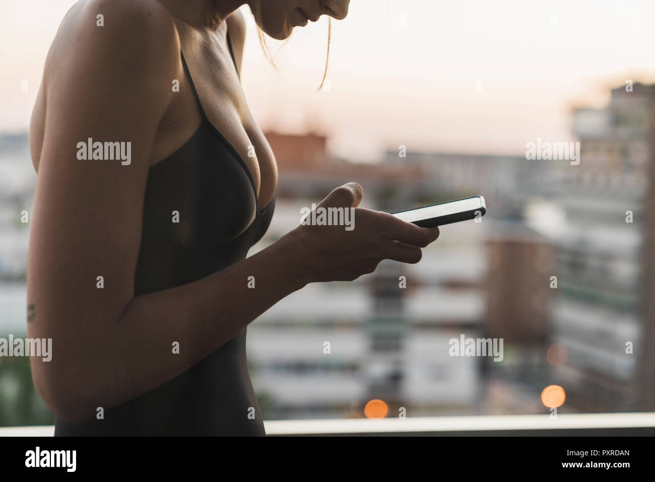 Close-up of young woman wearing black dress using cell phone on balcony Stock Photo