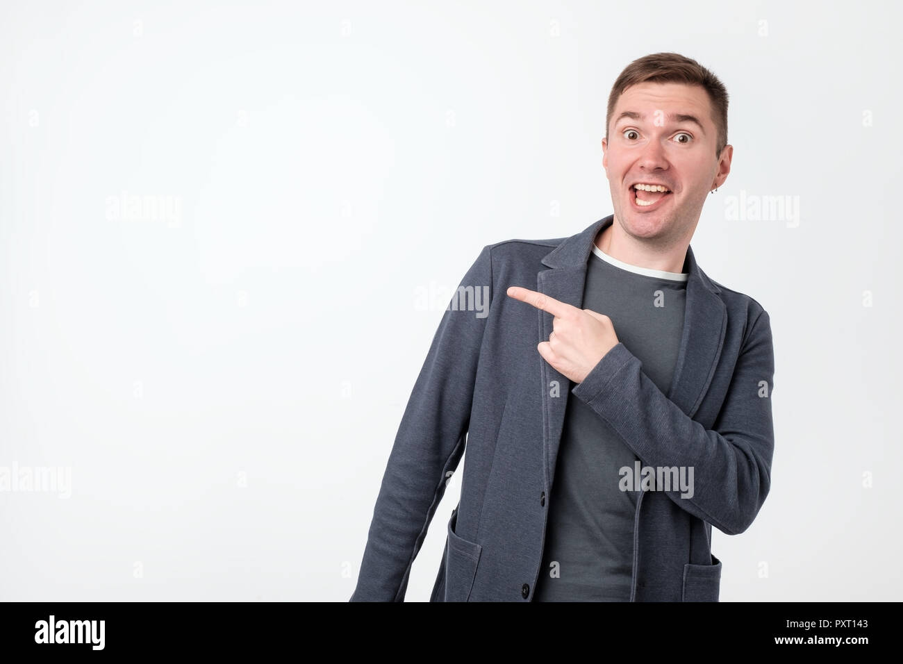 Handsome pensive guy with good-looking hairstyle looking aside and pointing with index finger. Copy space. Stock Photo