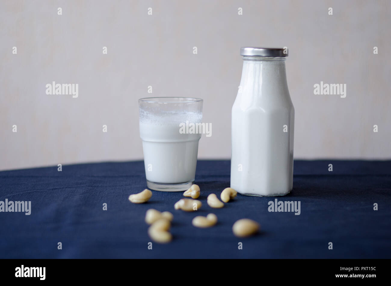Cashew nut milk bottle and glass standing together with ingredients in front. Stock Photo