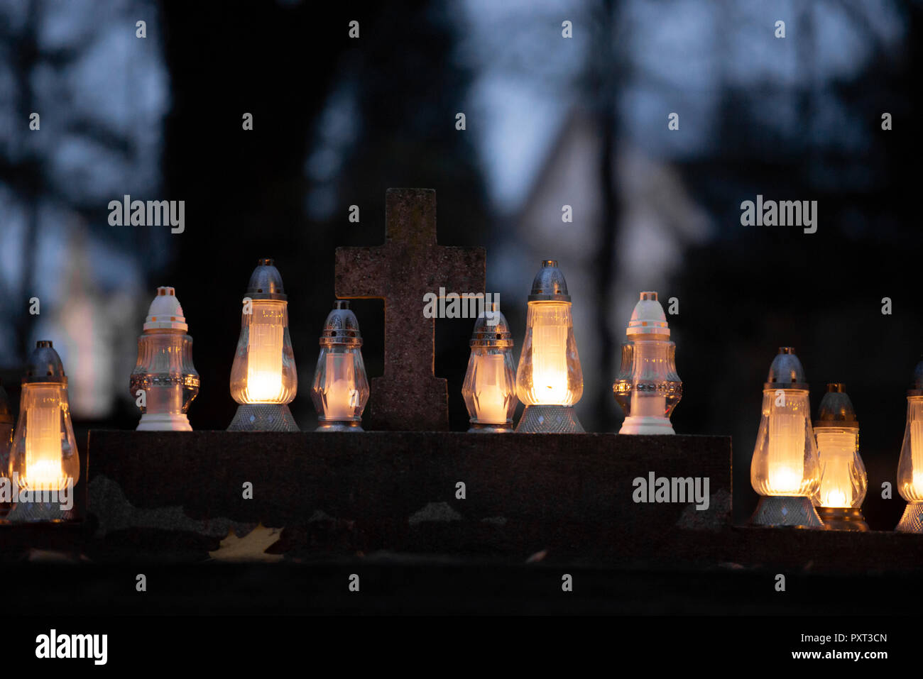 Yellow candles on the grave glowing in the dark around cross-relief. Celebrating All Saint's Day. Stock Photo