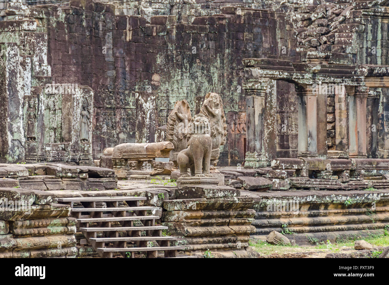 Unrestaured guardian statues of a Cambodian naga, garudas and a lion and bas-reliefs of devatas in the Bayon temple in Angkor Thom in Cambodia Stock Photo