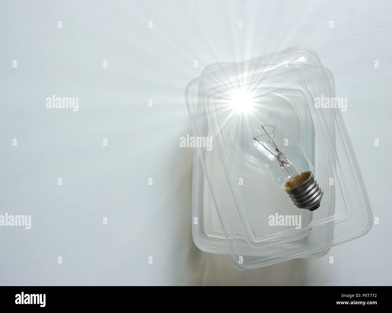 a light bulb with light spokes placed outside a clear box on white wooden surface, think outside a box concept Stock Photo