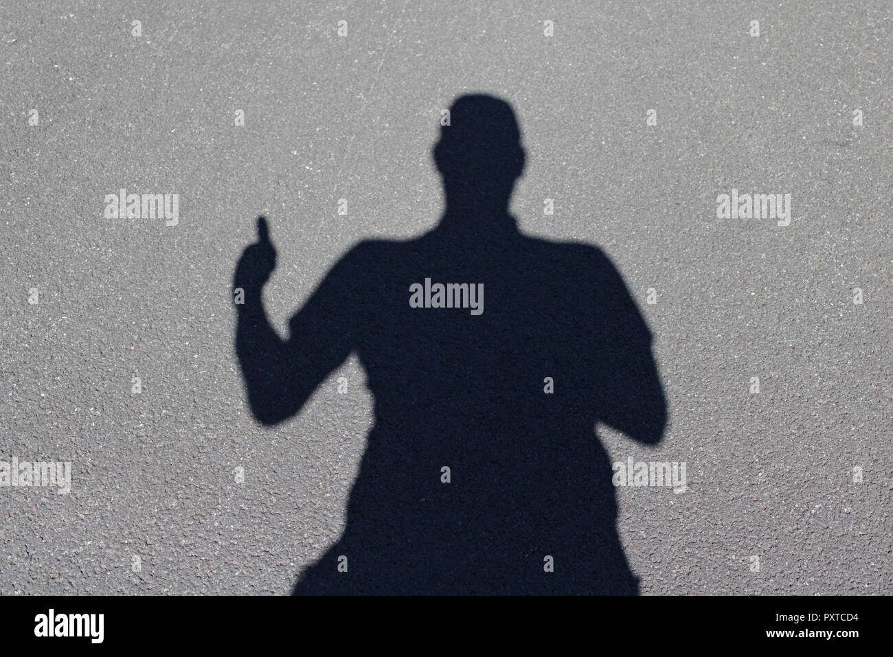 Human shadow on gray concrete ground giving the thumbs-up sign with one hand Stock Photo