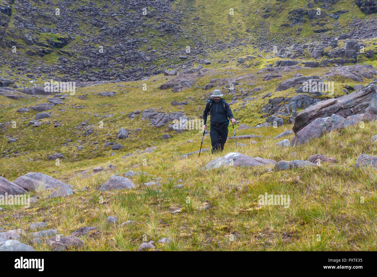 Scottish Highlands, UK - August 5, 2017: Solitude walker with backpack walking clothes hat and walking poles crossing a Scottish Highlands mountain me Stock Photo