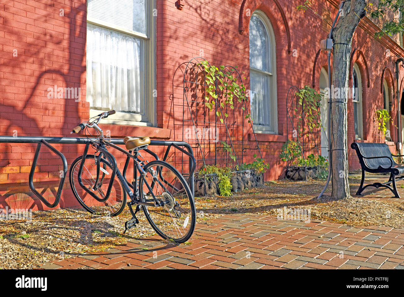 An early fall scene in Wiloughby, Ohio where a single bike is parked next to a russet orange building with a smattering of fallen autumn leaves. Stock Photo