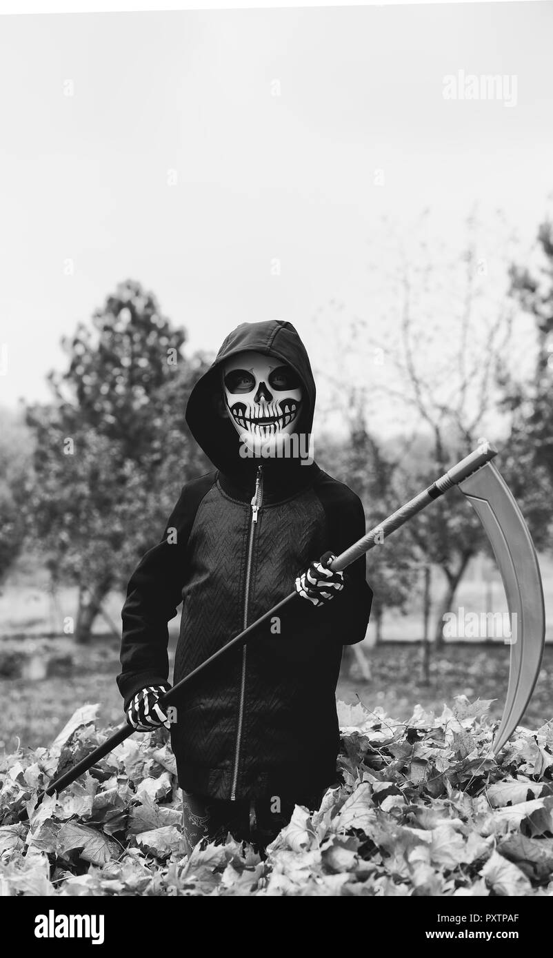 Child boy wears in scary Halloween skull skeleton mask with scythe in