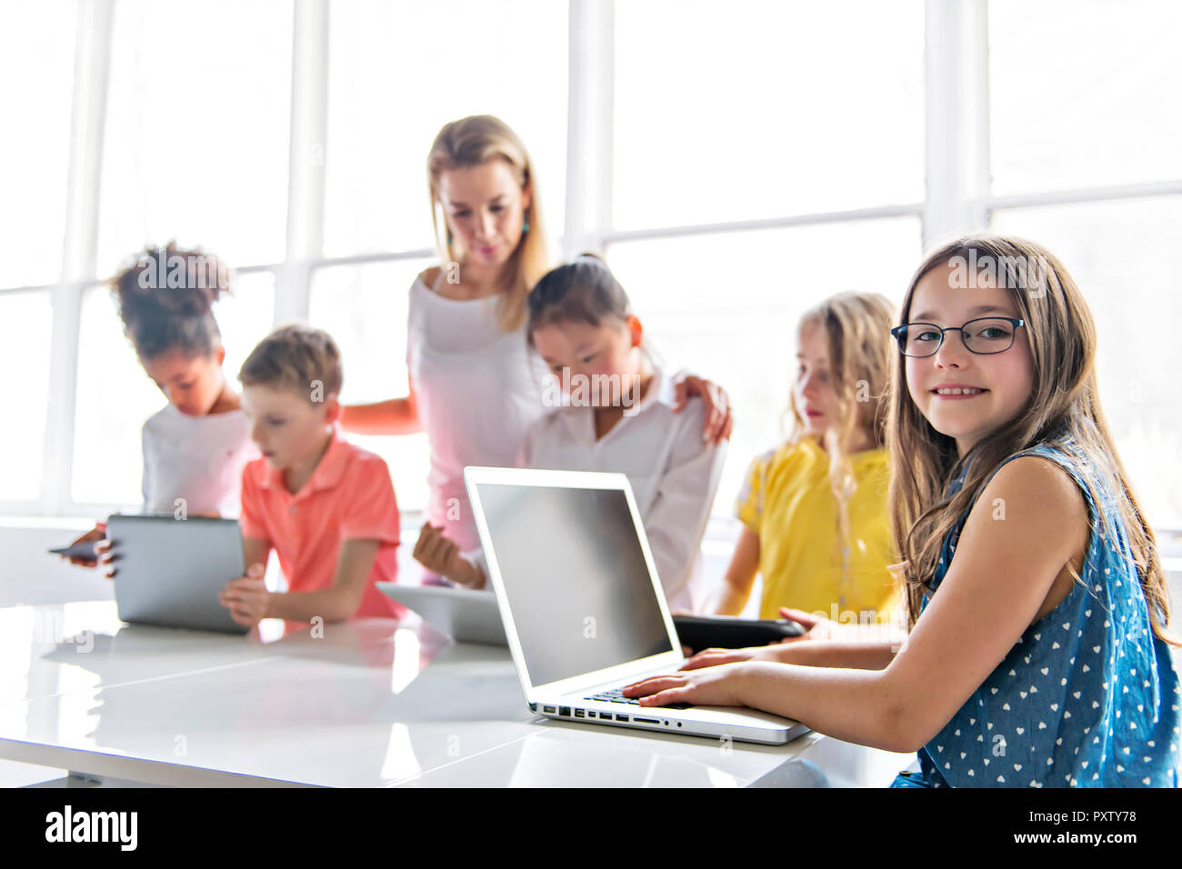 A child with technology tablet and laptop computer in classroom teacher ...