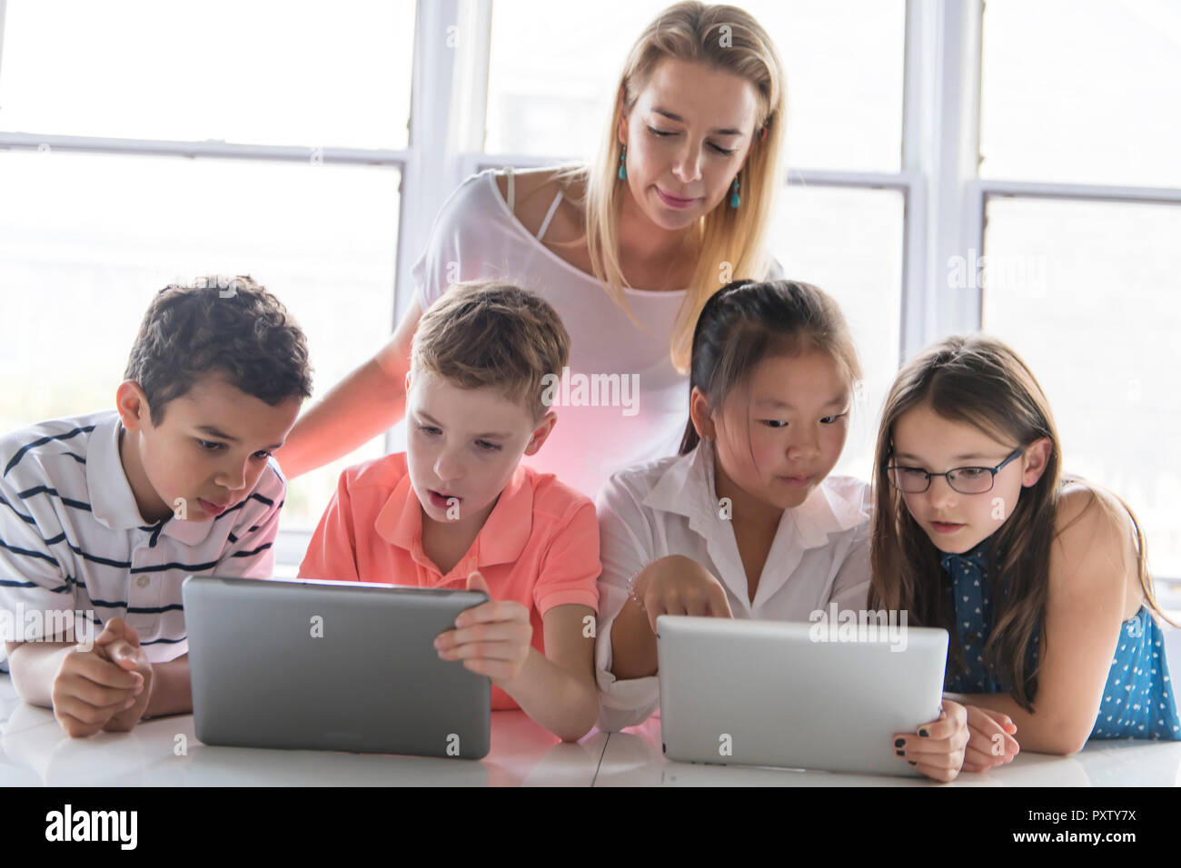A child with technology tablet and laptop computer in classroom teacher ...