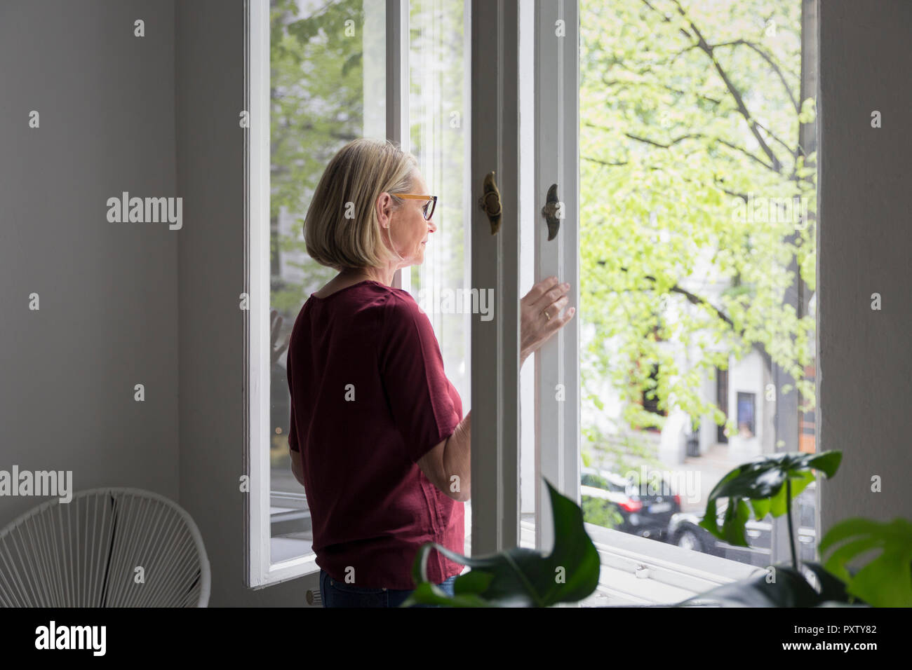 Mature woman at home opening the window Stock Photo