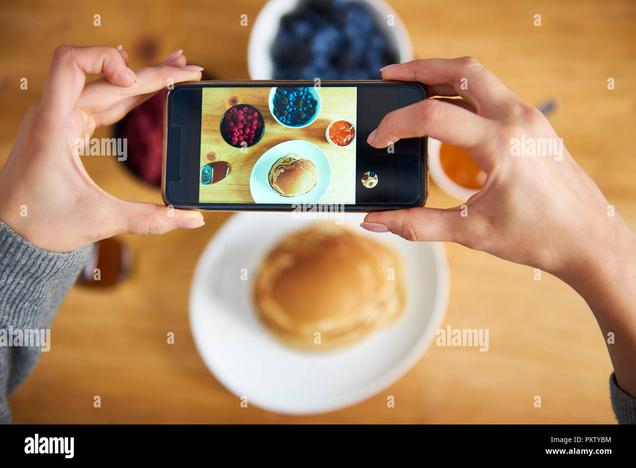 Young woman taking pictures of breakfast pancakes with berries and fresh fruit Stock Photo