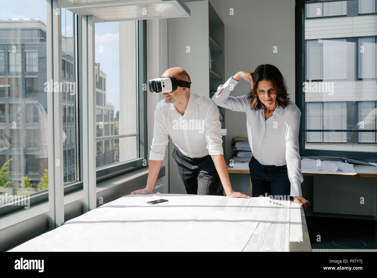 Two architects working on blueprints, man using VR glasses Stock Photo