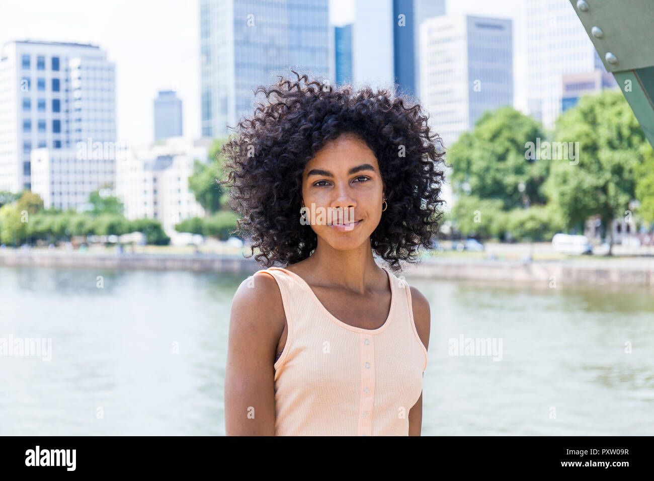 Germany, Frankfurt, portrait of relaxed young woman with curly hair in front of Main River Stock Photo