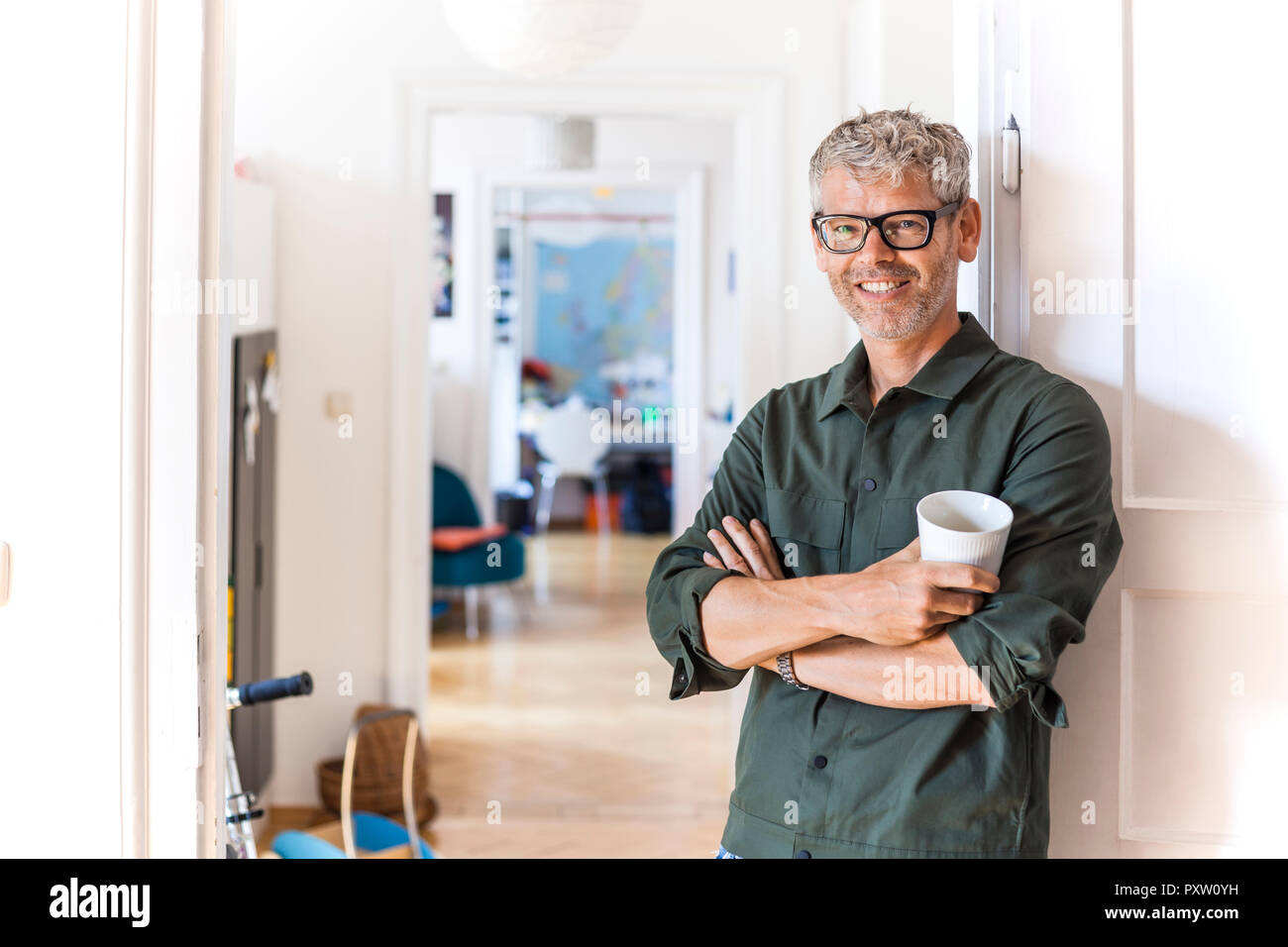 Portrait of smiling mature man with coffee cup leaning against door case at home Stock Photo