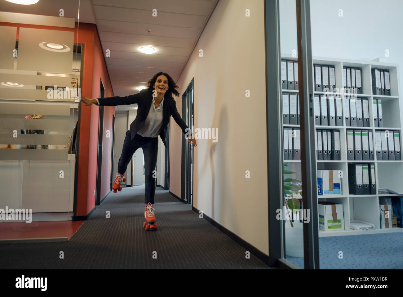 Mature businesswoman rollerskating in office corridor Stock Photo