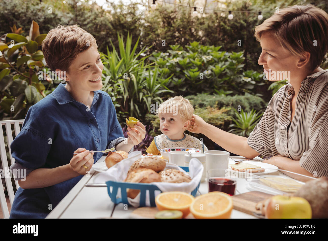 Two happy mothers at breakfast table outdoors with their child Stock Photo