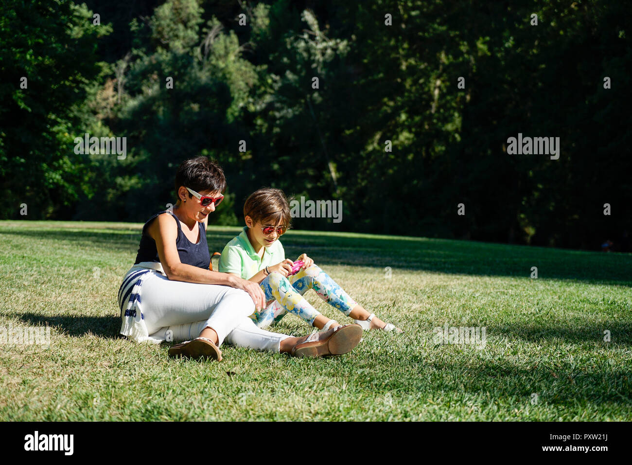 Mother and daughter taking photographs, sitting on grass Stock Photo