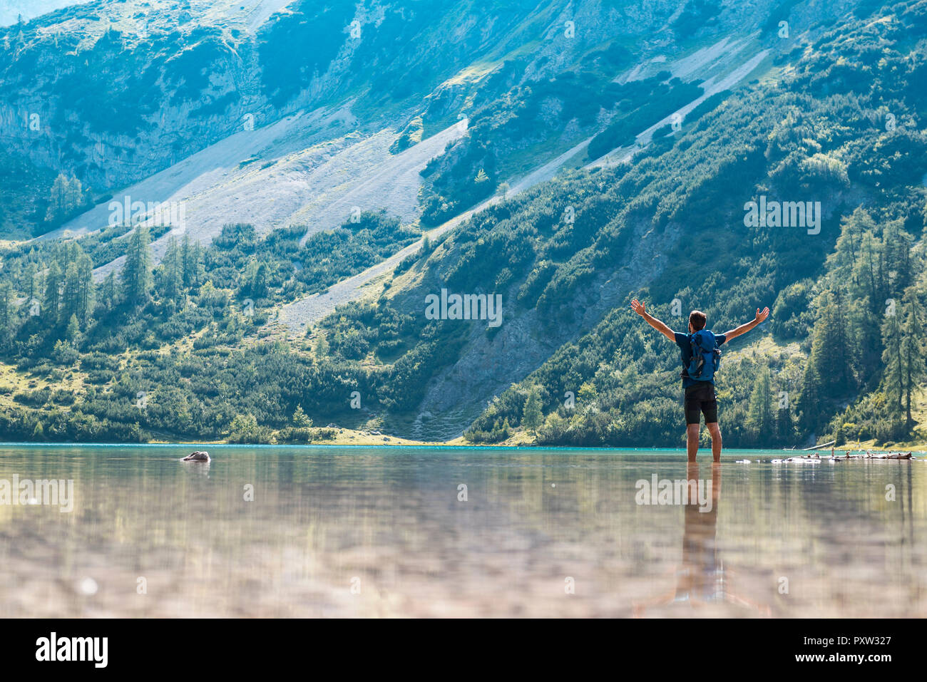 Austria, Tyrol, Hiker at Lake Seebensee standing ankle deep in water, with raised arms Stock Photo