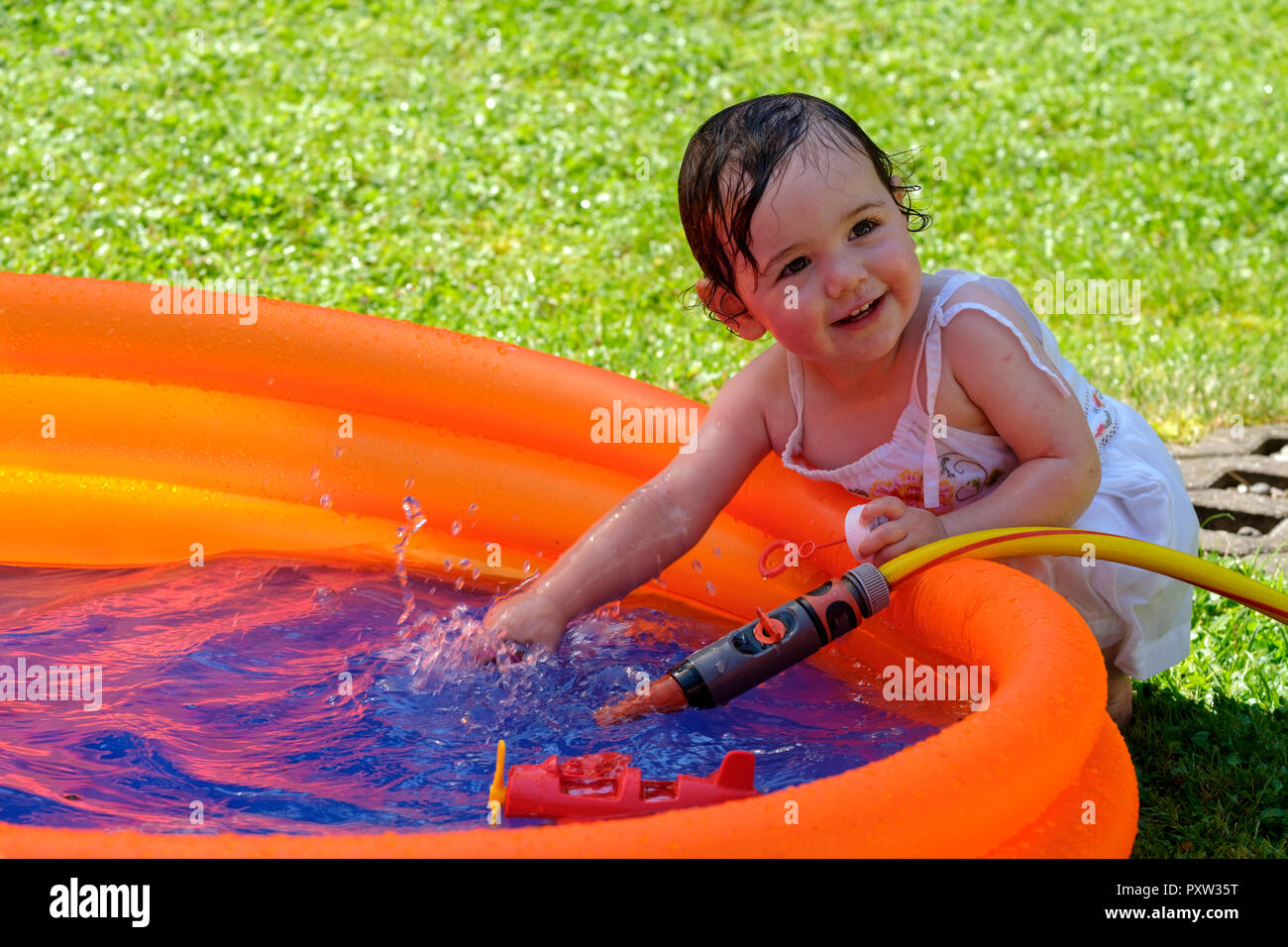 Portrait of smiling baby girl splashing with water in a paddling pool in the garden Stock Photo