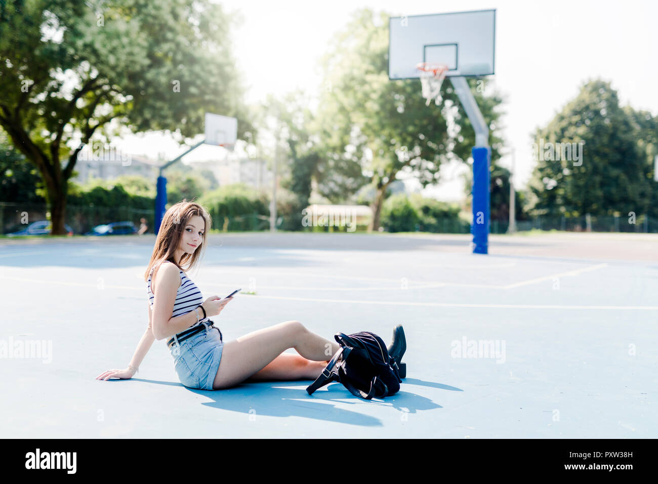 Portrait of young woman with backpack sitting on sports ground with cell phone Stock Photo