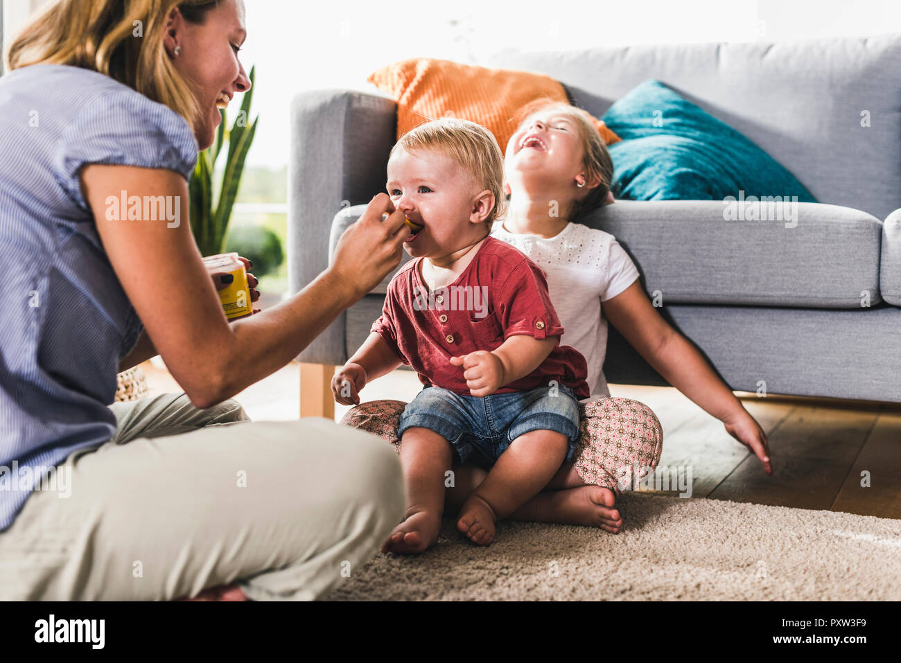 Mother feeding kids in living room Stock Photo