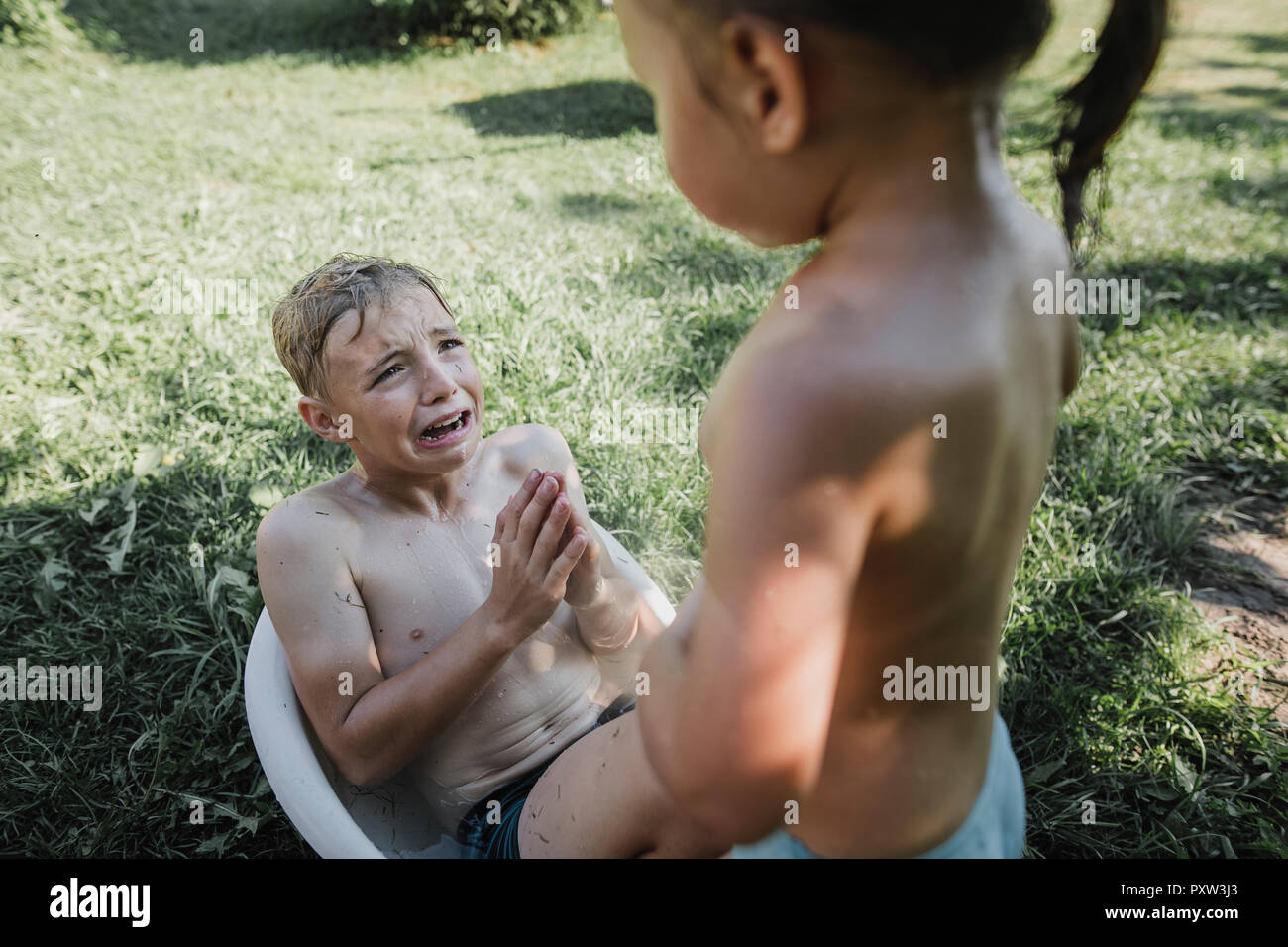 Brother and sister playing with water in little bath tub in garden Stock Photo