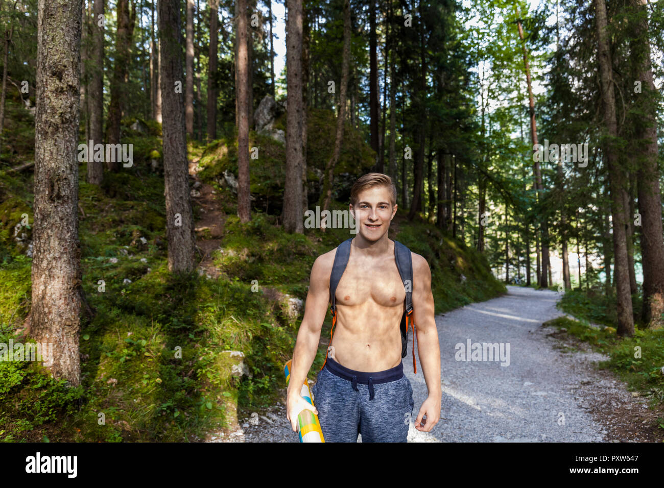 Germany, Bavaria, portrait of shirtless young man with backpack standing on forest track Stock Photo