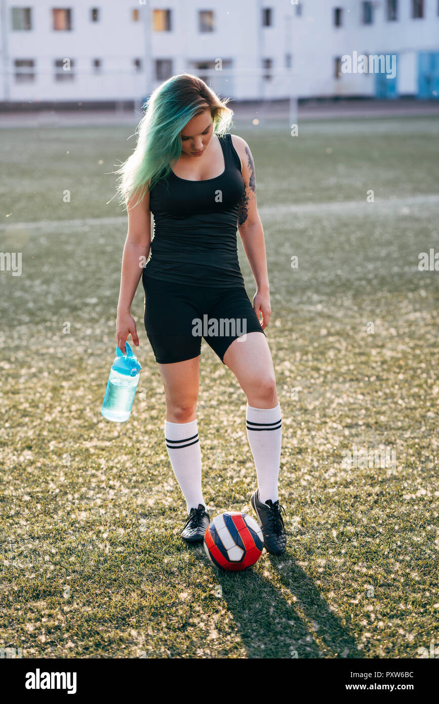 Young woman standing on football ground with ball and bottle of water Stock Photo