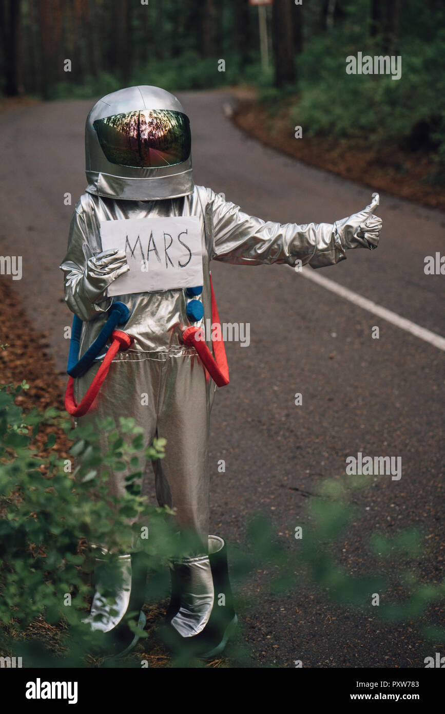 Spaceman hitchhiking to Mars, standing on road in forest Stock Photo