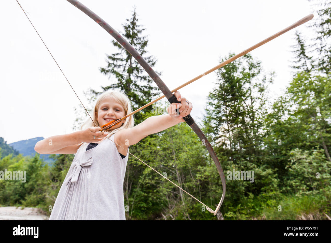 Smiling girl aiming with bow and arrow in the nature Stock Photo