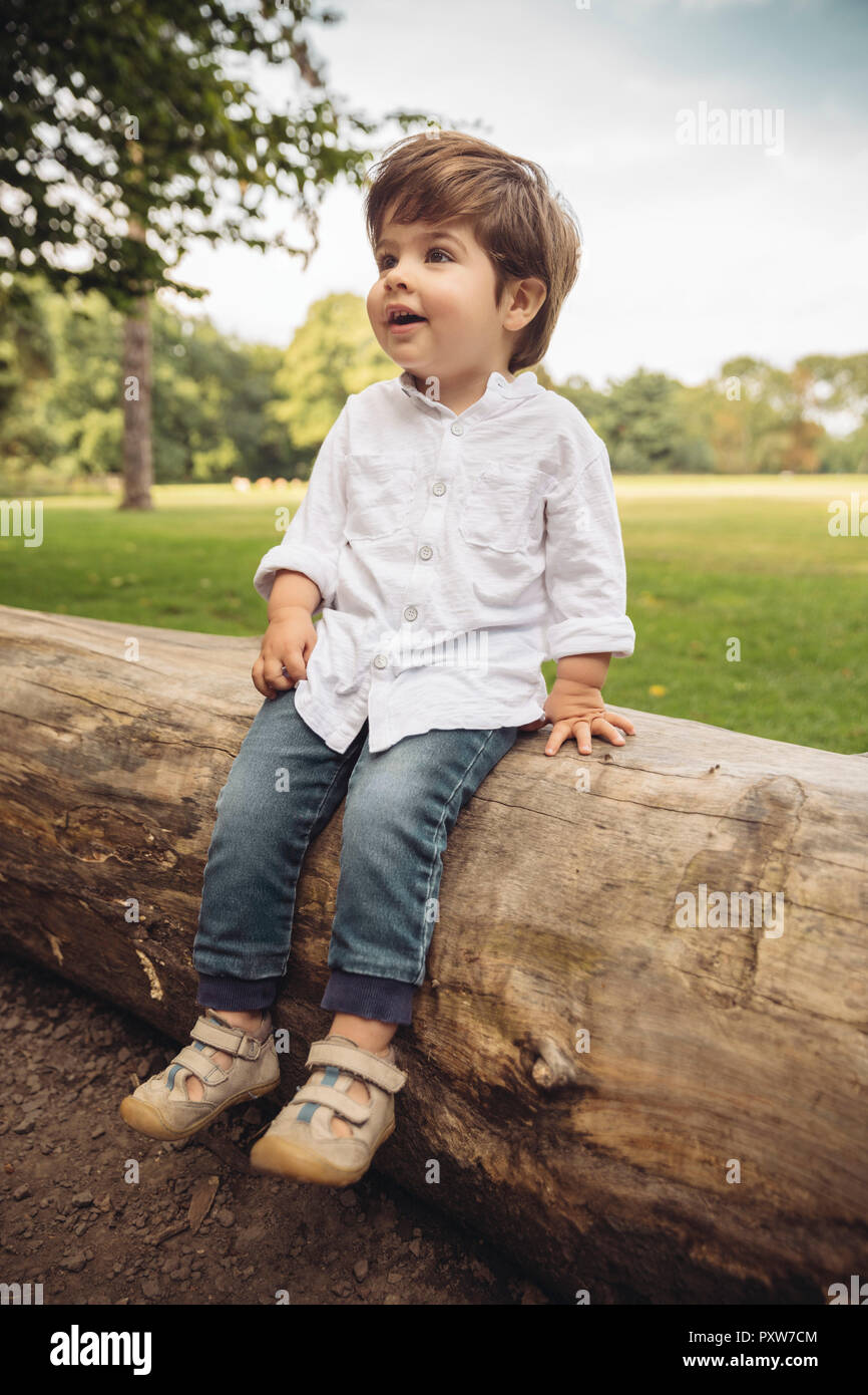 Happy toddler sitting on tree trunk in park Stock Photo
