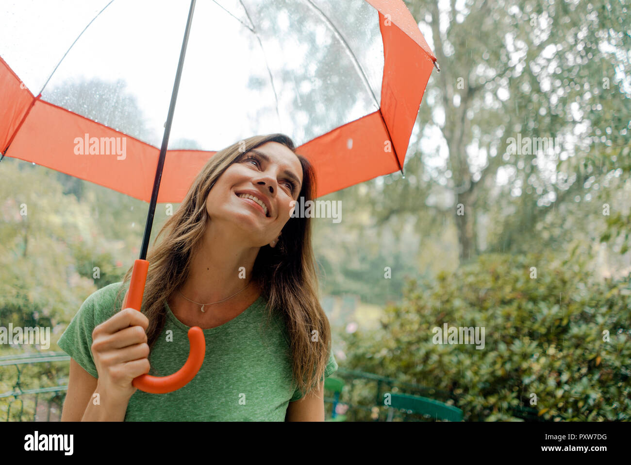 Smiling mature woman standing in rain under umbrella Stock Photo