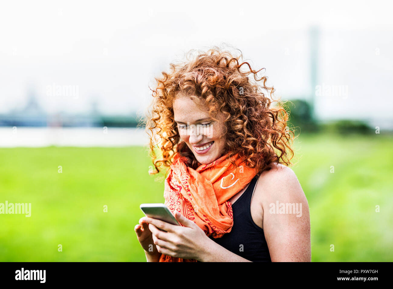 Portrait of happy young woman with curly red hair looking at cell phone Stock Photo