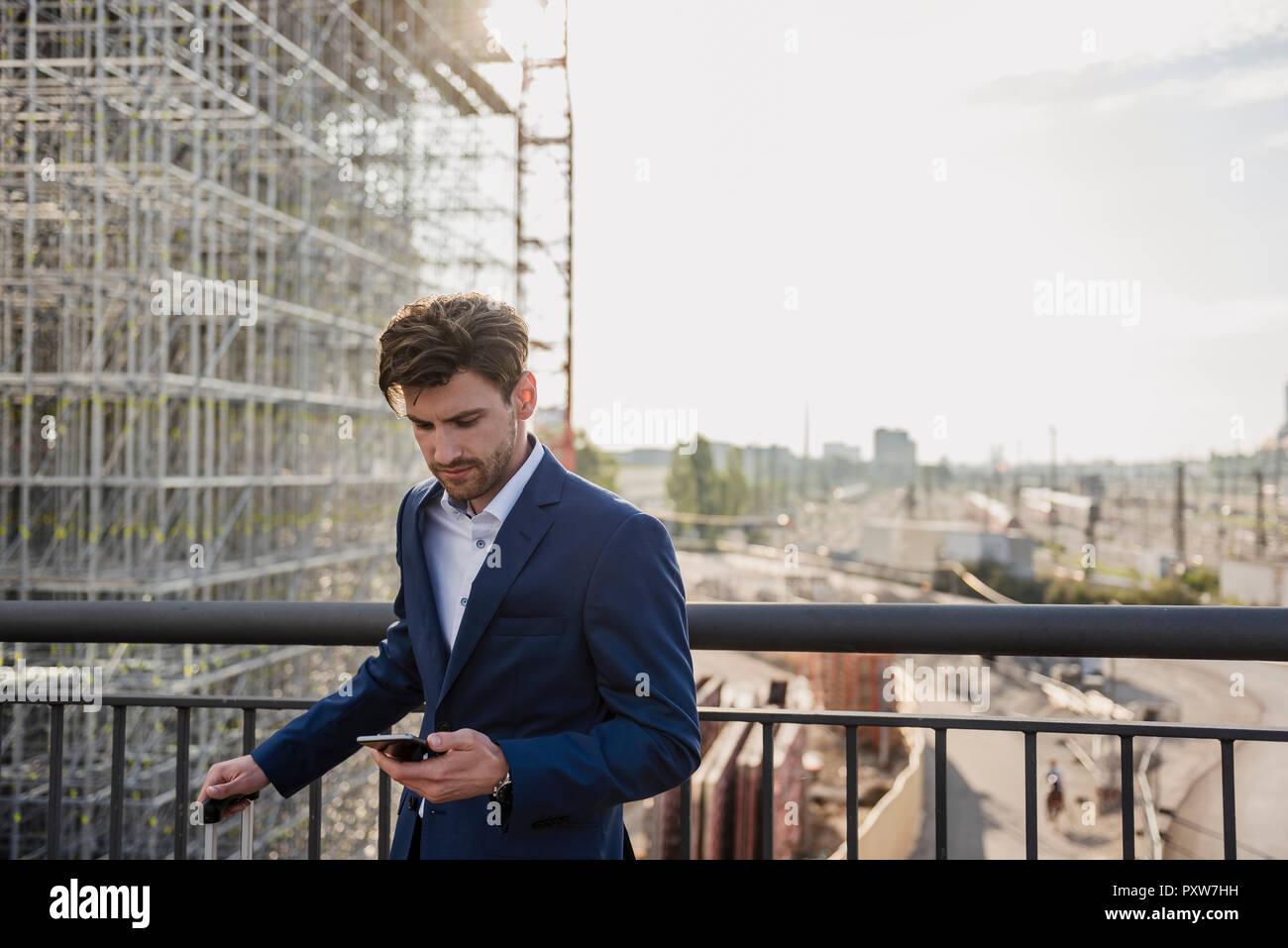 Businessman standing on bridge in the city using cell phone Stock Photo