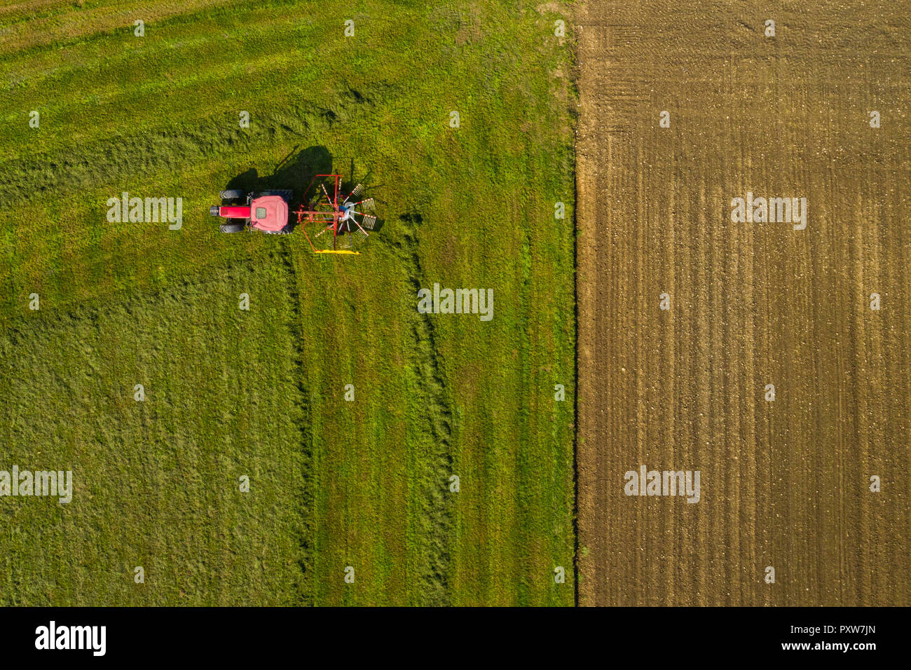 Top down aerial view of a red tractor cultivating farmland with a spinning blade in rural Slovenia Stock Photo