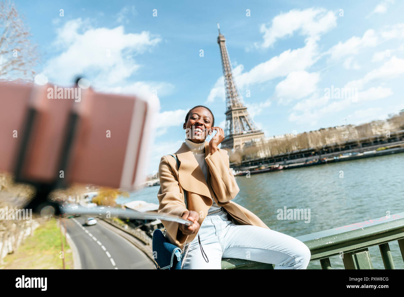 France, Paris, Woman sitting on bridge over the river Seine with the Eiffel tower in the background taking a selfie Stock Photo