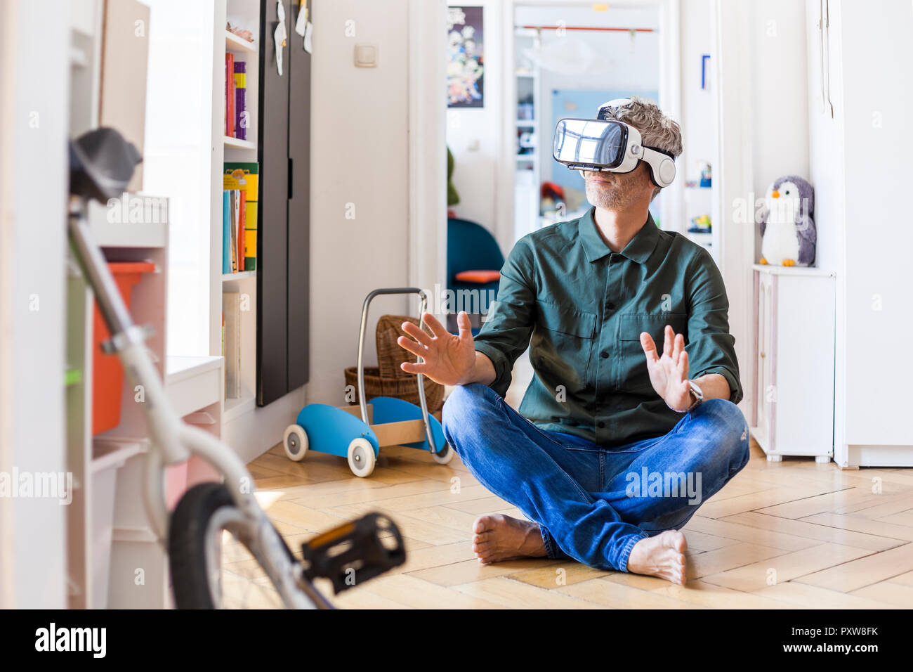 Mature man sitting on the floor at home using Virtual Reality Glasses Stock Photo