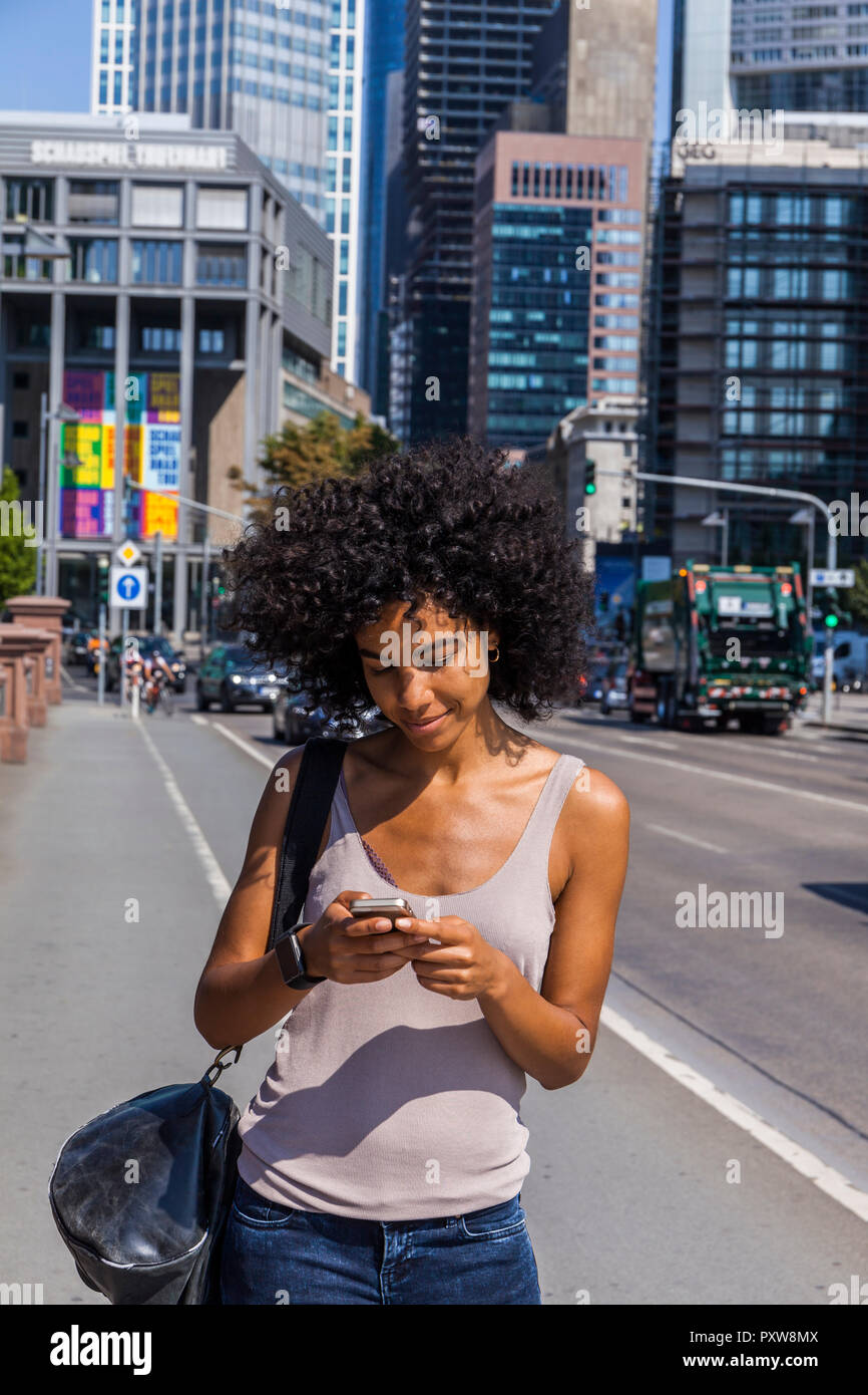 Germany, Frankfurt, smiling young woman with curly hair using cell phone Stock Photo