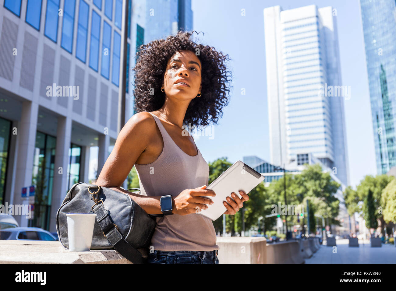 Germany, Frankfurt, portrait of young woman with travelling bag, tablet and coffee to go in the city Stock Photo