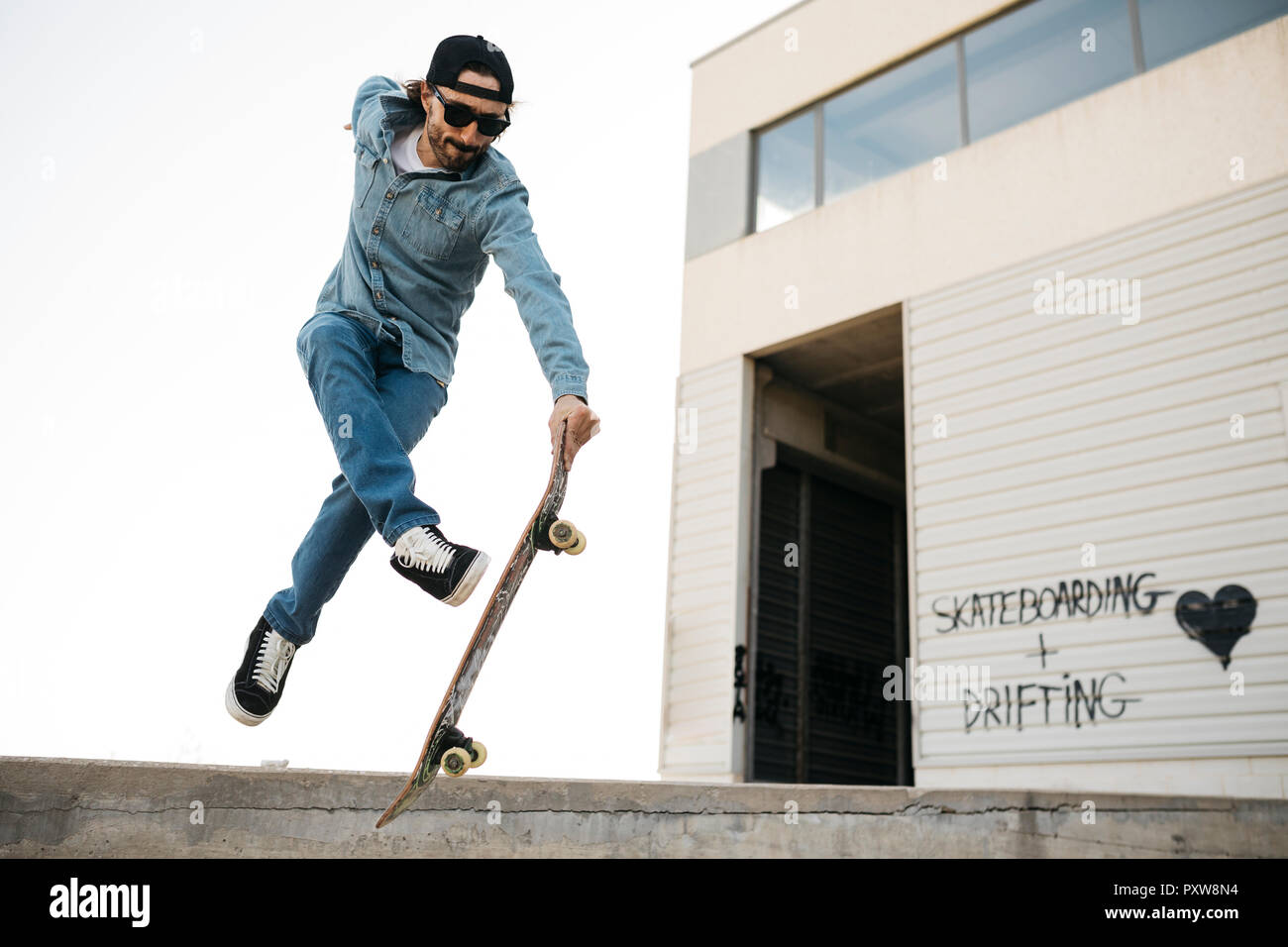 Trendy man in denim and cap skateboarding, doing jump with skateboard